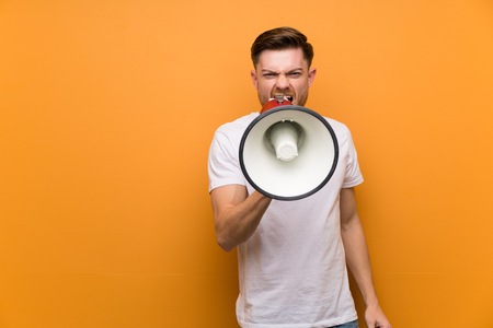 Redhead man over brown wall shouting through a megaphoneの写真素材
