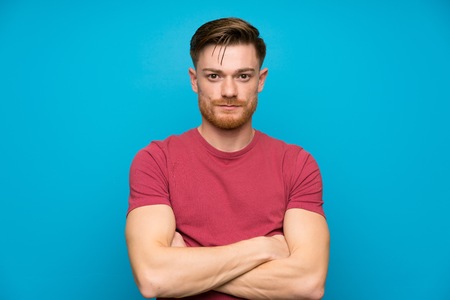 Redhead man on isolated blue wall keeping arms crossedの写真素材