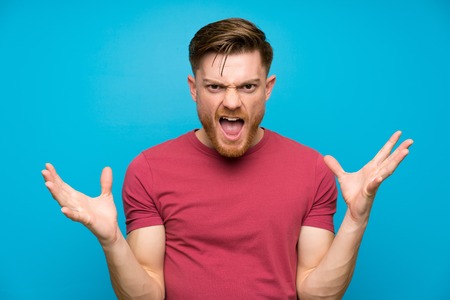 Redhead man on isolated blue wall unhappy and frustrated with somethingの写真素材