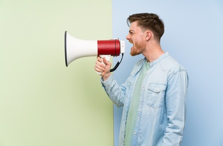 Redhead man over colorful background shouting through a megaphoneの写真素材