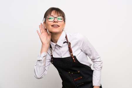Young woman with apron listening to something by putting hand on the ear