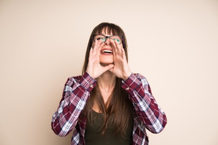 Young woman on ocher background shouting with mouth wide open