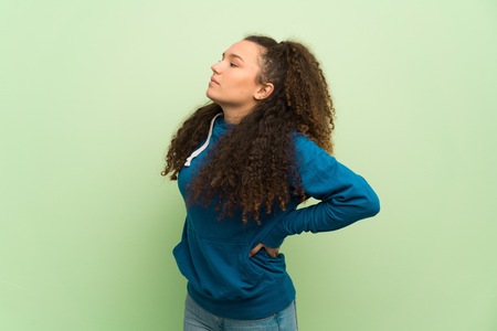 Teenager girl over green wall suffering from backache for having made an effort