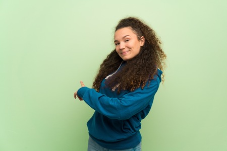 Teenager girl over green wall pointing back with the index fingerの写真素材