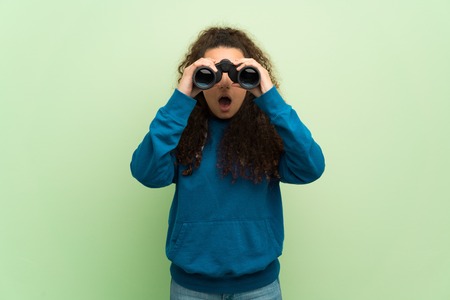Teenager girl over green wall and looking in the distance with binocularsの写真素材