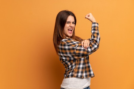 Young woman over brown wall doing strong gesture