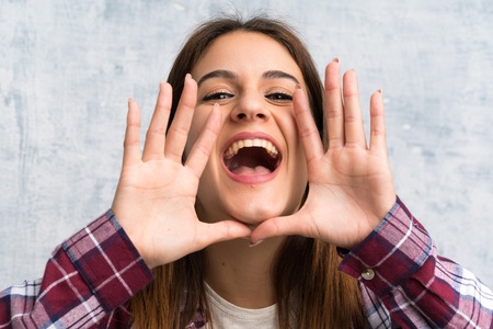 Young woman over textured wall shouting with mouth wide openの写真素材