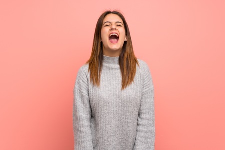 Young woman over pink wall shouting to the front with mouth wide openの写真素材