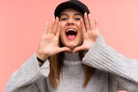 Fashion woman with hat over pink wall shouting with mouth wide openの写真素材