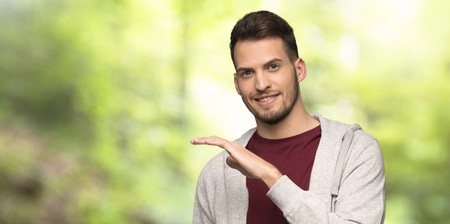 Man with sweatshirt holding copyspace to insert an ad in a parkの写真素材