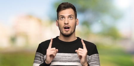 Handsome man pointing up and surprised at outdoorsの写真素材