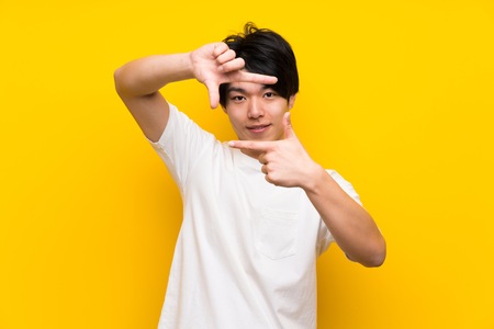 Asian man over isolated yellow wall focusing face. Framing symbolの写真素材
