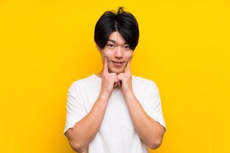 Asian man over isolated yellow wall smiling with a happy and pleasant expressionの写真素材