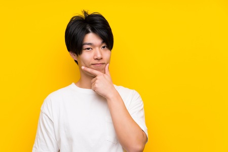Asian man over isolated yellow wall thinkingの写真素材