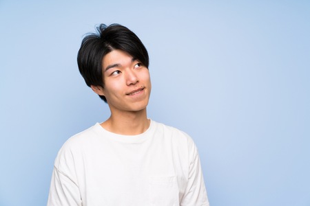 Asian man on isolated blue background laughing and looking upの写真素材