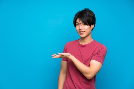 Asian man with red shirt over isolated blue wall extending hands to the side for inviting to comeの写真素材