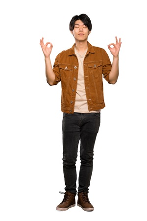 A full-length shot of a Asian man with brown jacket in zen pose over isolated white backgroundの写真素材
