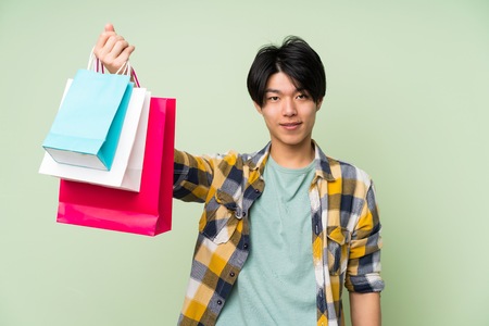 Asian man over isolated green wall holding a lot of shopping bagsの写真素材