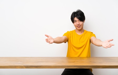 Asian man with yellow shirt presenting and inviting to come with handの写真素材