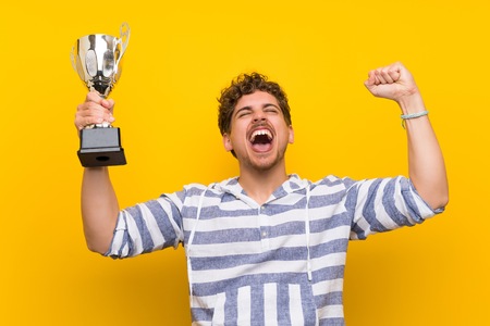 Blonde man over yellow wall holding a trophyの写真素材