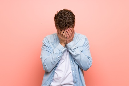 Blonde man over pink wall with tired and sick expression