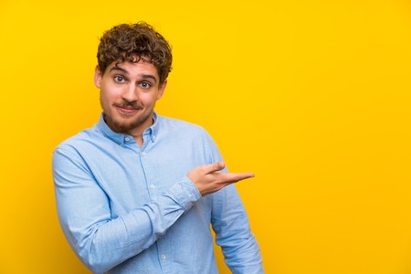 Blonde man over isolated yellow wall extending hands to the side for inviting to comeの写真素材