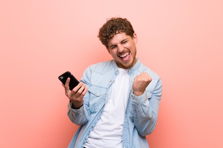 Blonde man over pink wall celebrating a victory with a mobileの写真素材