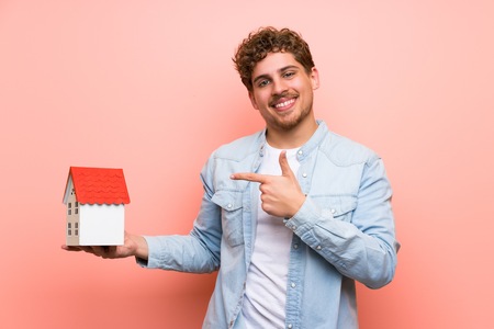 Blonde man over pink wall holding a little houseの写真素材