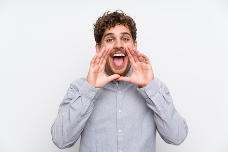 Blonde man over isolated white wall shouting with mouth wide openの写真素材