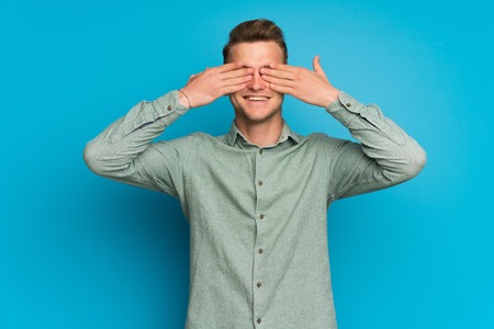 Blonde man over isolated blue wall covering eyes by handsの写真素材
