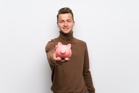 Blonde man over isolated white wall holding a piggybankの写真素材