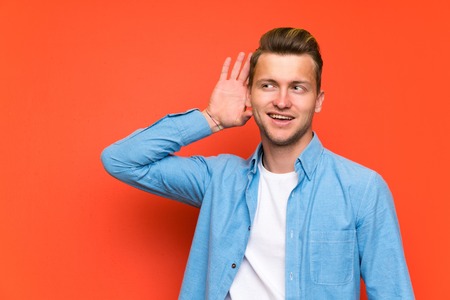 Blonde handsome man over isolated wall listening somethingの写真素材