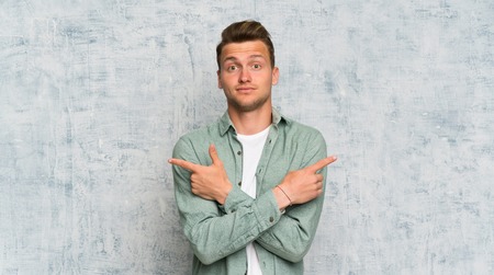 Blonde handsome man with green shirt pointing to the laterals having doubtsの写真素材