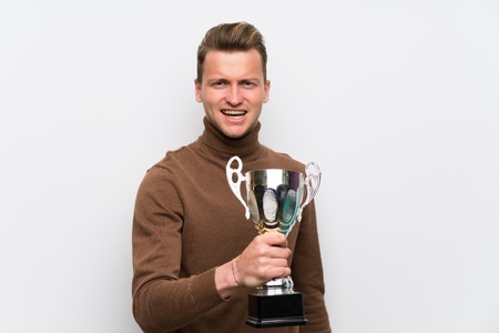 Blonde man over isolated white wall holding a trophyの写真素材