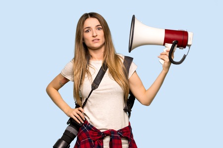 Young photographer woman taking a megaphone that makes a lot of noise on isolated blue background