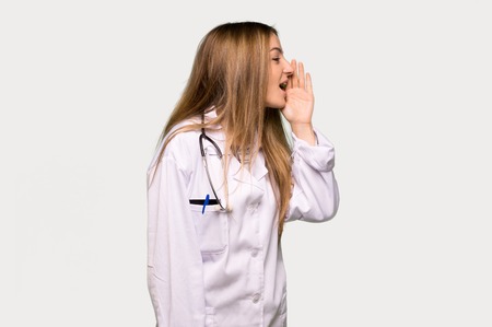 Young doctor woman shouting with mouth wide open to the lateral on isolated grey backgroundの写真素材