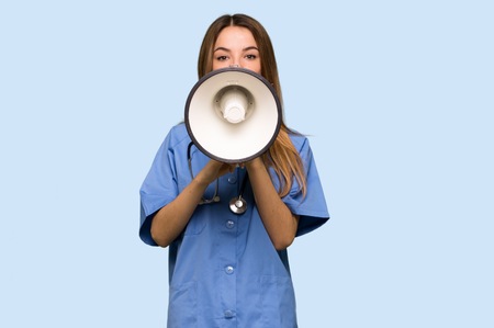 Young nurse shouting through a megaphone to announce something on isolated blue backgroundの写真素材