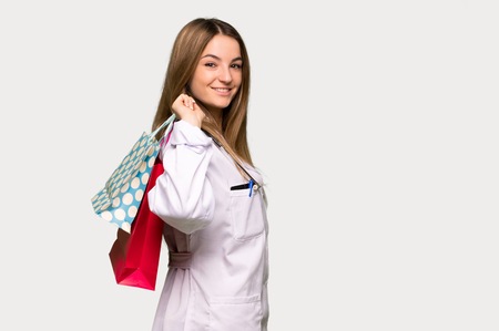 Young doctor woman holding a lot of shopping bags on isolated grey backgroundの写真素材