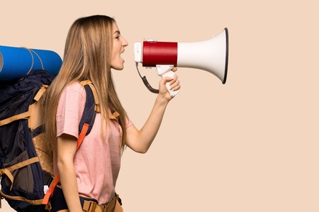 Young backpacker woman shouting through a megaphone to announce something in lateral position on isolated yellow backgroundの写真素材