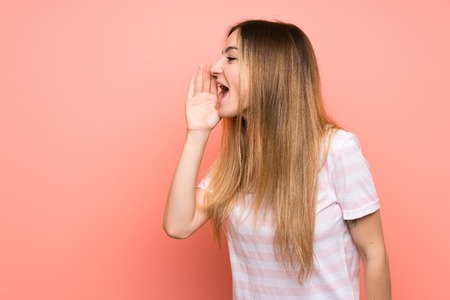 Young woman over isolated pink wall shouting with mouth wide openの写真素材