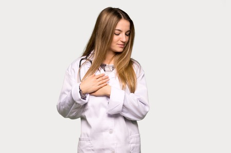 Young doctor woman having a pain in the heart on isolated grey backgroundの写真素材
