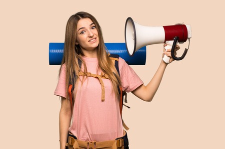 Young backpacker woman taking a megaphone that makes a lot of noise on isolated yellow backgroundの写真素材