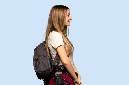 Young photographer woman in lateral position on isolated blue background