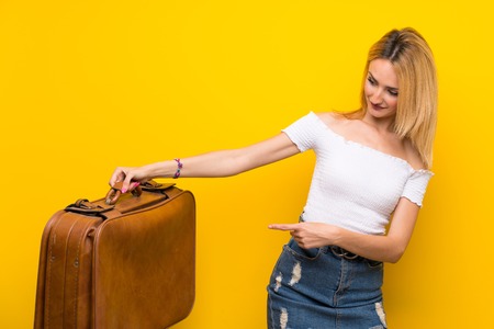 Young blonde woman over isolated yellow wall holding a vintage briefcaseの写真素材