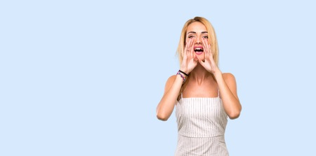 Young blonde woman shouting and announcing something over isolated blue background