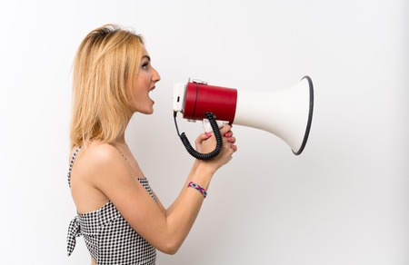 Young blonde woman over isolated white shouting through a megaphoneの写真素材