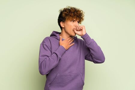 Young african american man over isolated green wall is suffering with cough and feeling badの写真素材