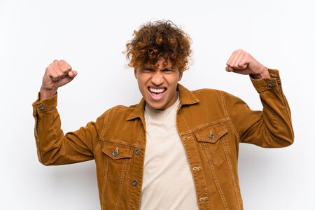 Young african american man over isolated white wall celebrating a victoryの写真素材