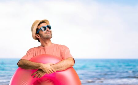 Man with hat and sunglasses on his summer vacation stand and looking up while smiling at the beachの写真素材