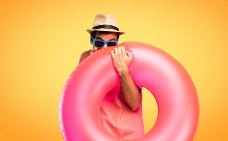 Man with hat and sunglasses on his summer vacation pointing with finger at someone and laughing a lot while covering mouth on orange backgroundの写真素材